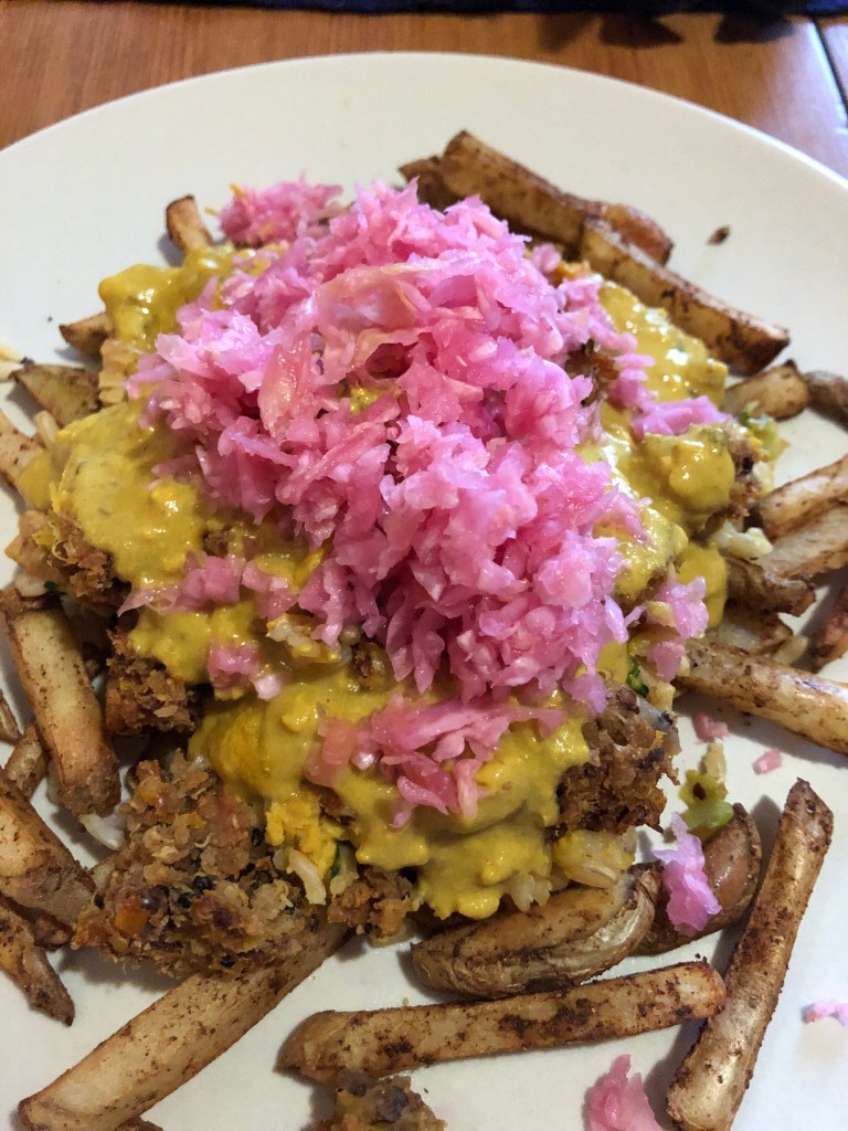 fries topped with crumbled burger, kale, cheesy sauce and pink sauerkraut
