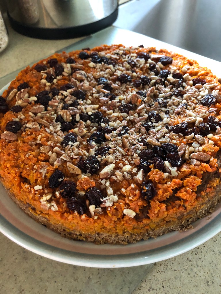 carrot halwa cake on a plate. Round cake with caramelized carrots, raisins, and pecan pieces on top