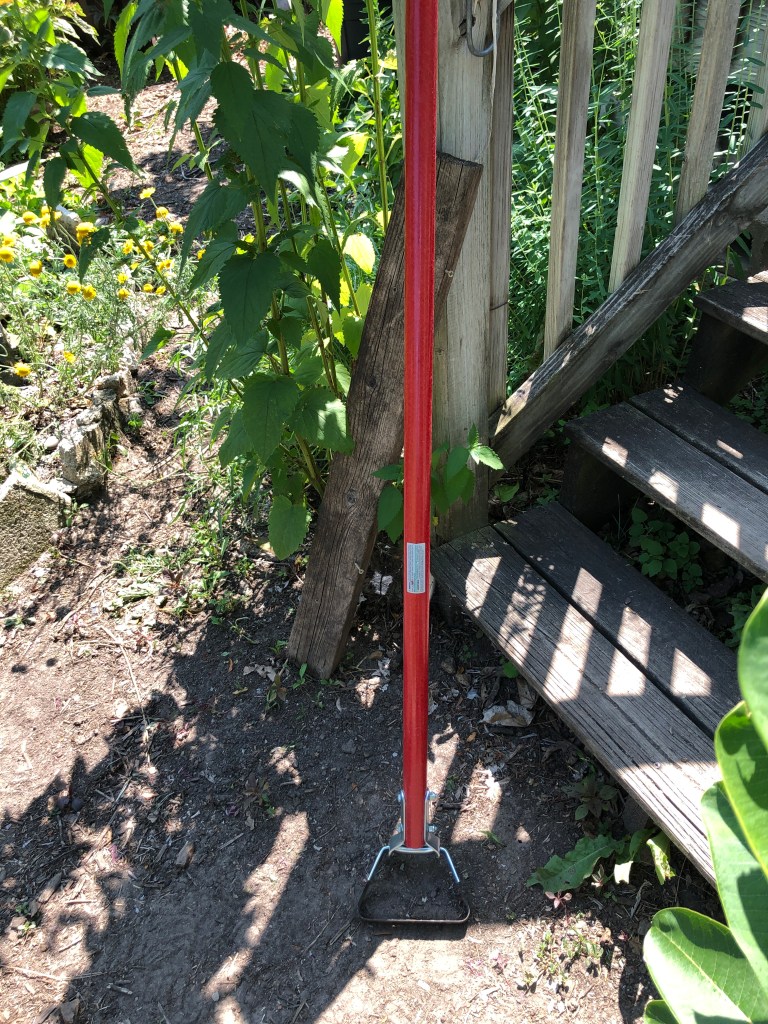 scuffle hoe with a long red handle leaning up against the bottom newel post on some wooden steps