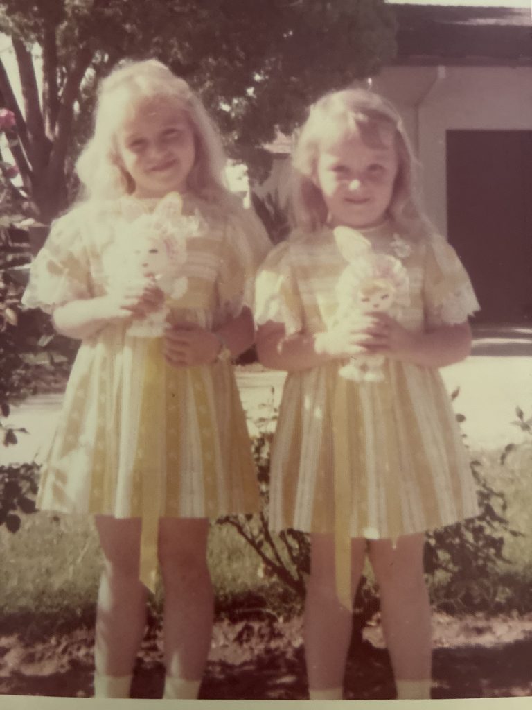 Two girls in yellow and white dresses hold Easter rabbit dolls